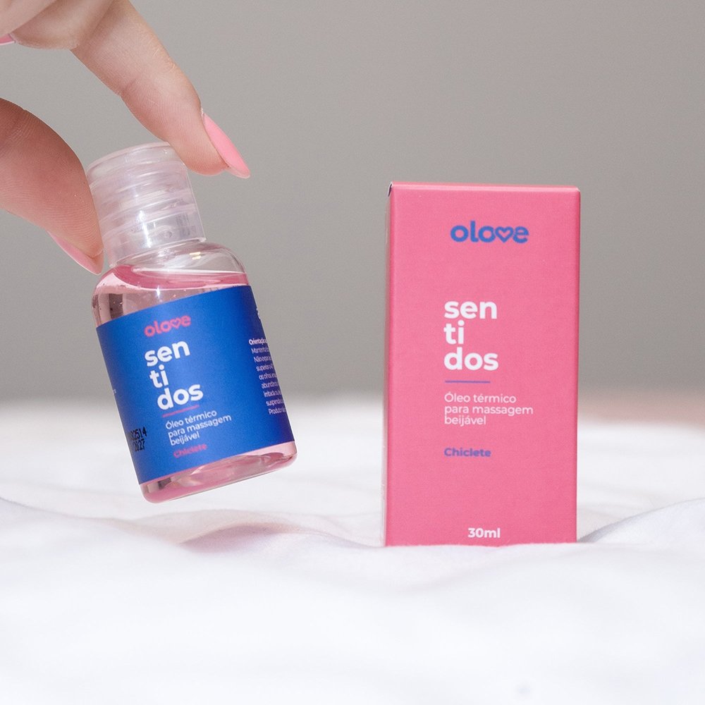 Mulher segurando o frasco do �leo para Massagem Sensual Olove Sentidos Chiclete 30ml e sua embalagem, em ambiente �ntimo