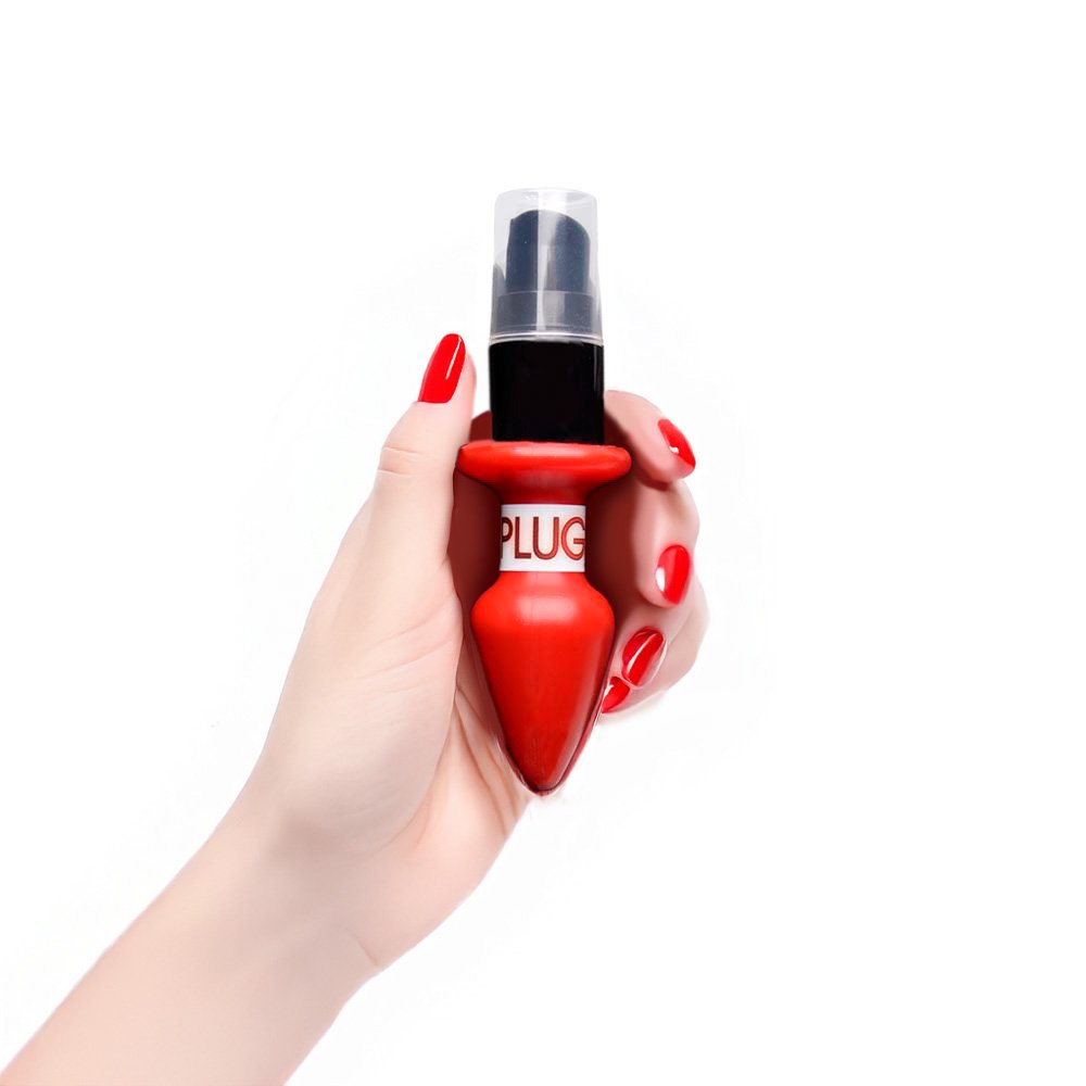 M�o feminina segurando o Vibrador L�quido Beij�vel Aroma e Sabor Morango do Amor 15ml, com anel preto ao redor da base, unhas vermelhas.