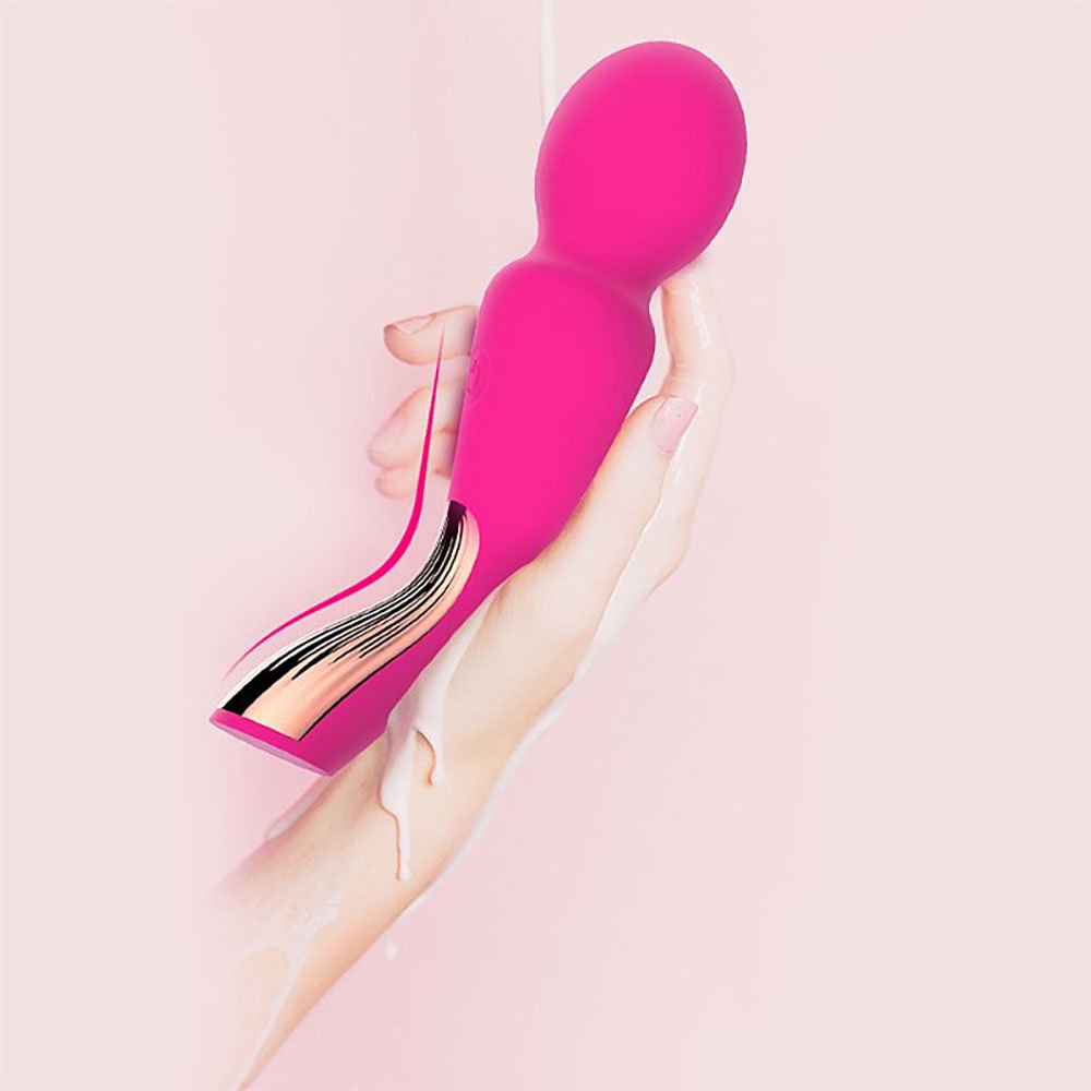 Massageador Wand Varinha M�gica Pink sendo segurado por uma mao, com um detalhe dourado na base, sobre um fundo rosa claro que remete a sensacoes