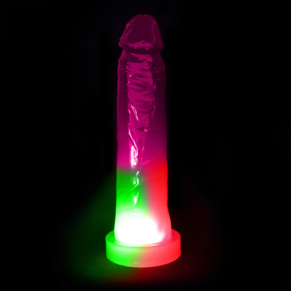 P�nis Pisca Pisca Jueves com Base para Cinta Transl�cido 19 x 4,5cm Rosa - Foto 01: Dildo rosa transl�cido com luzes verdes e vermelhas piscando na base sob fundo escuro
