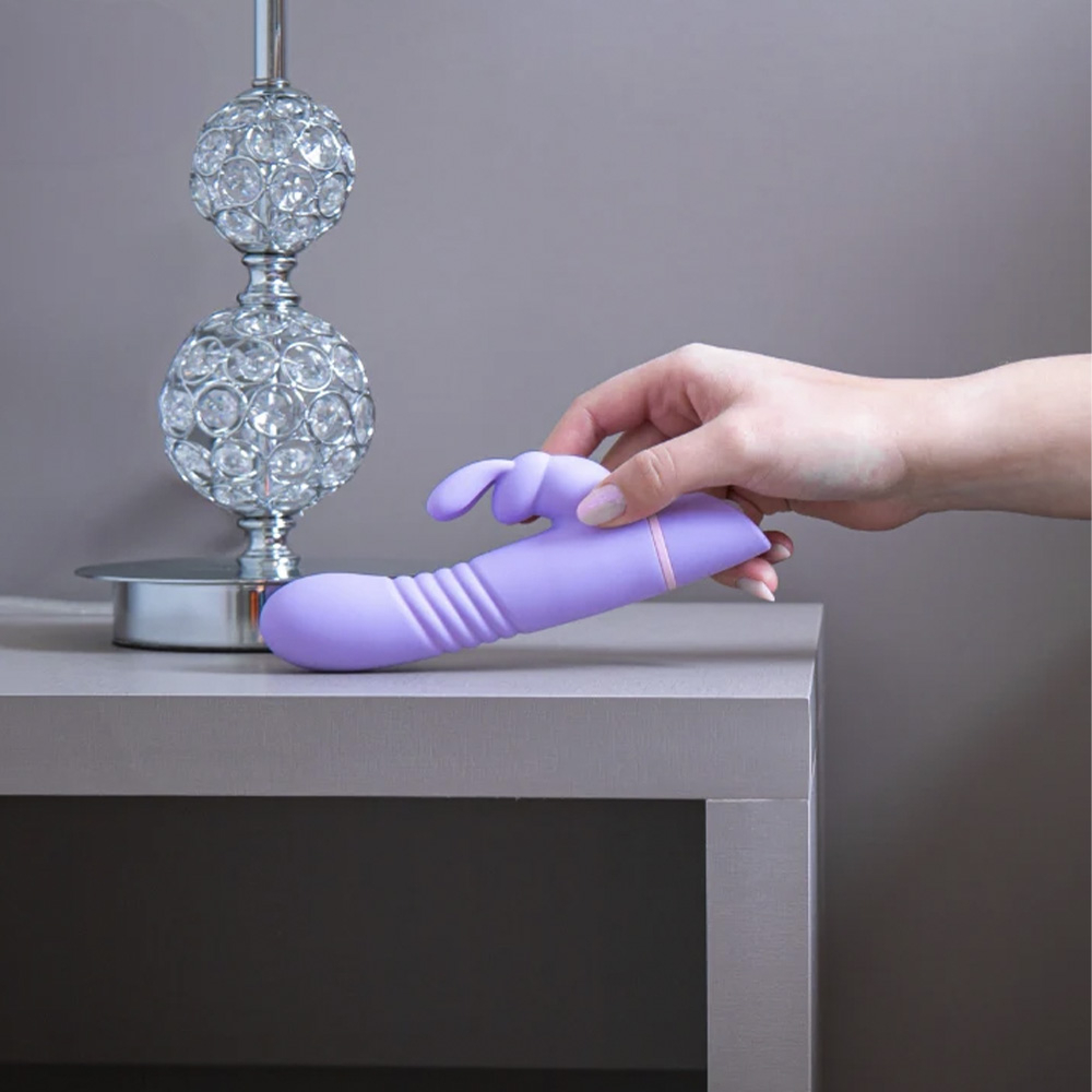 Vibrador Rabbit Recarreg�vel Revira Lil�s, Foto em ambiente decorado com a m�o de uma pessoa segurando o vibrador em uma c�moda, mostrando o design ergon�mico.