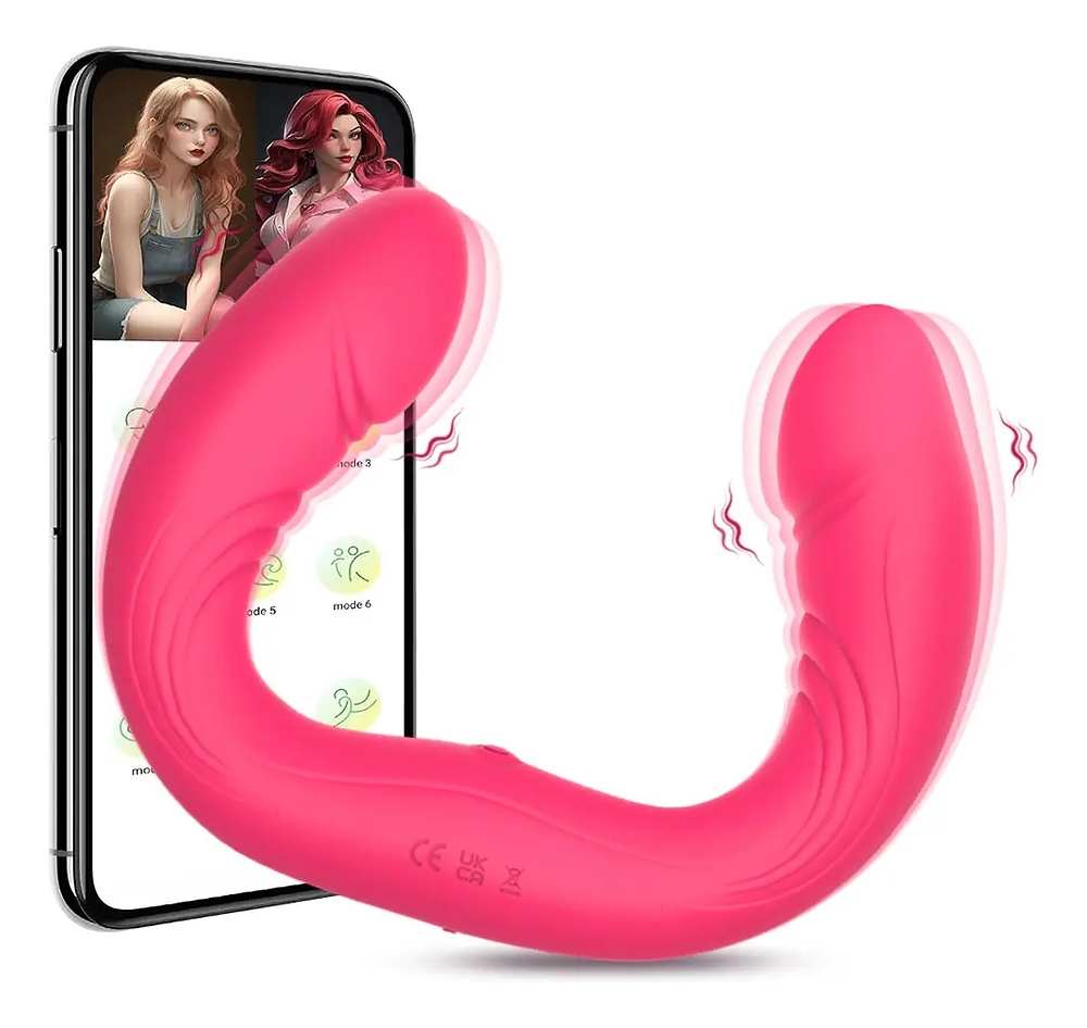 Vibrador duplo em silicone pink, visto de perfil, em formato de U com a base de carregamento e um smartphone ao fundo mostrando as op��es de modo de vibra��o