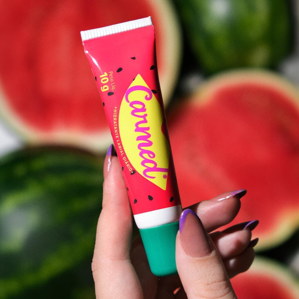 Hidratante Labial Carmed Incolor Aroma de Melancia 10g na m�o, com fundo desfocado de melancias cortadas.