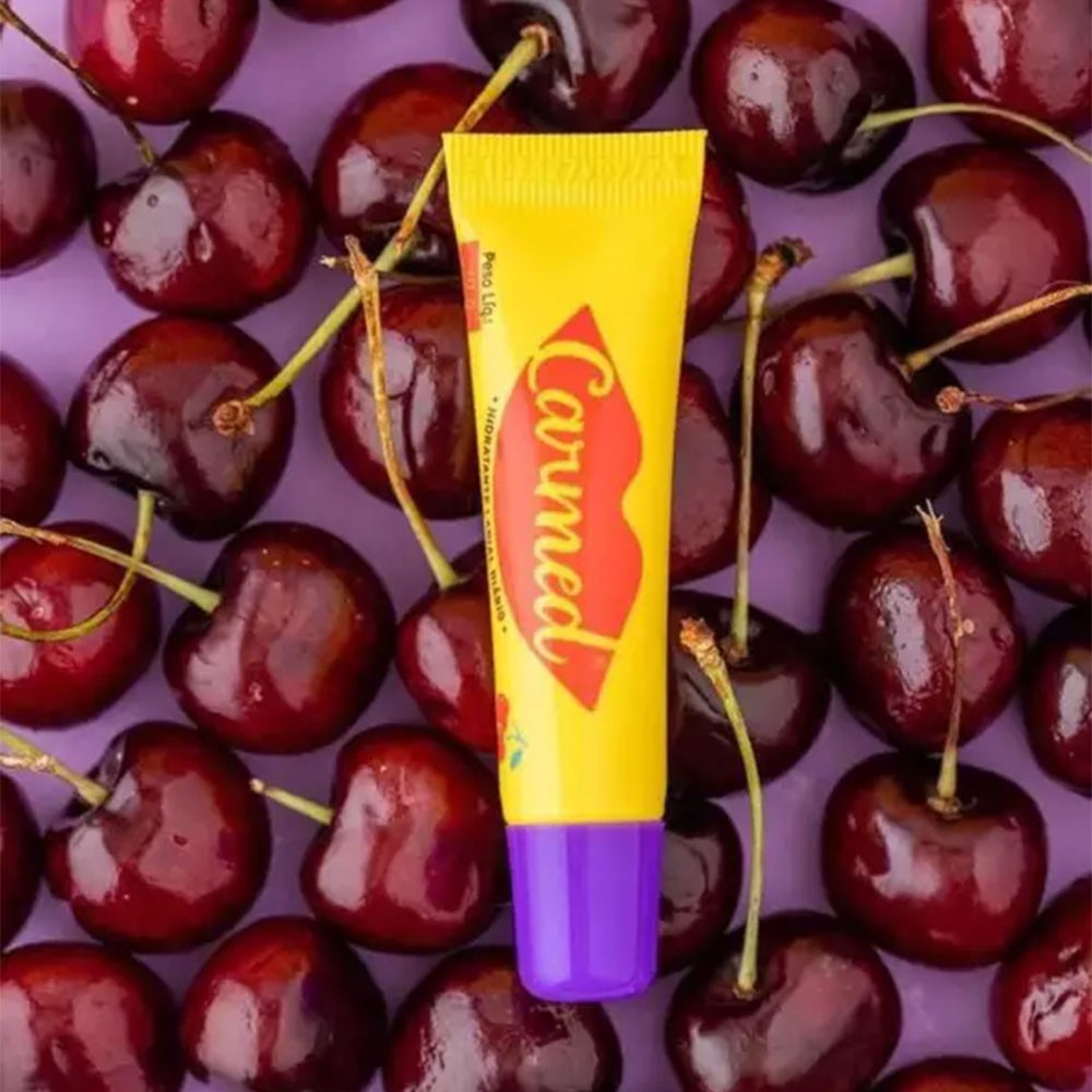 Carmed Incolor Aroma de Cereja 10g cercado por cerejas, mostrando a embalagem amarela com detalhes em roxo na tampa