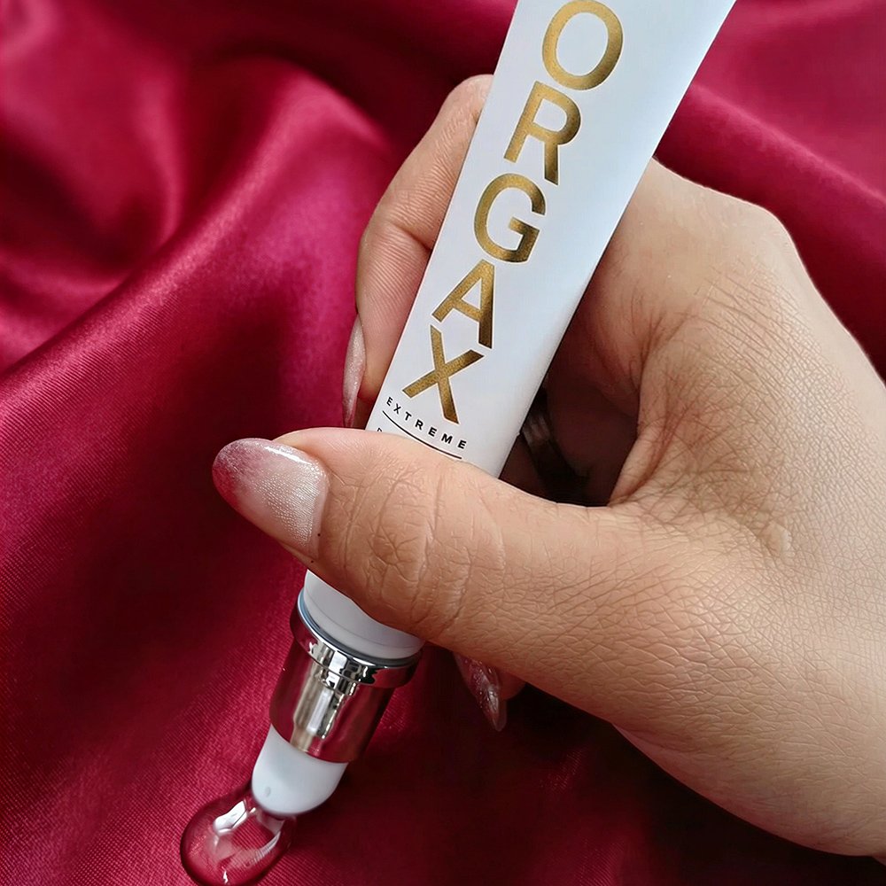 Close de uma m�o feminina aplicando o Gel Excitante Feminino Orgax sobre um tecido de seda vermelha, mostrando a textura do gel.