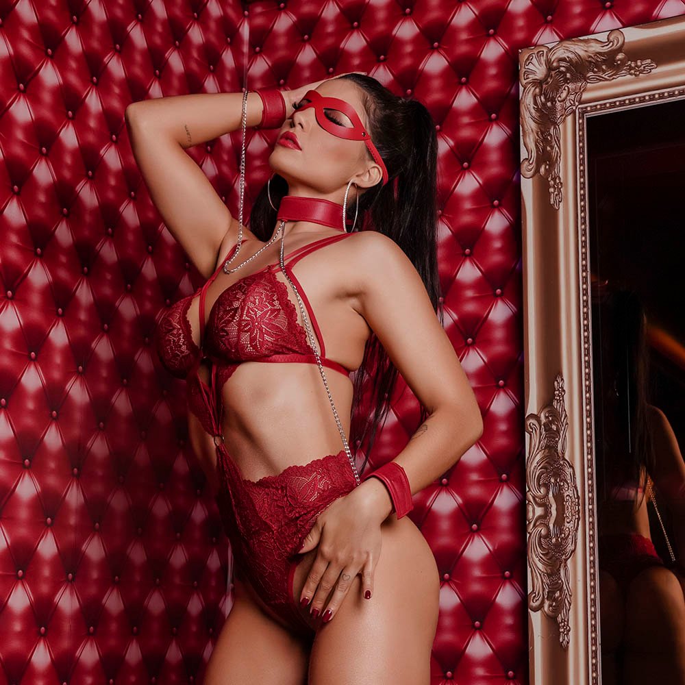 Body sensual vermelho em renda com coleira e algemas, modelo sentada de lado com bumbum em destaque